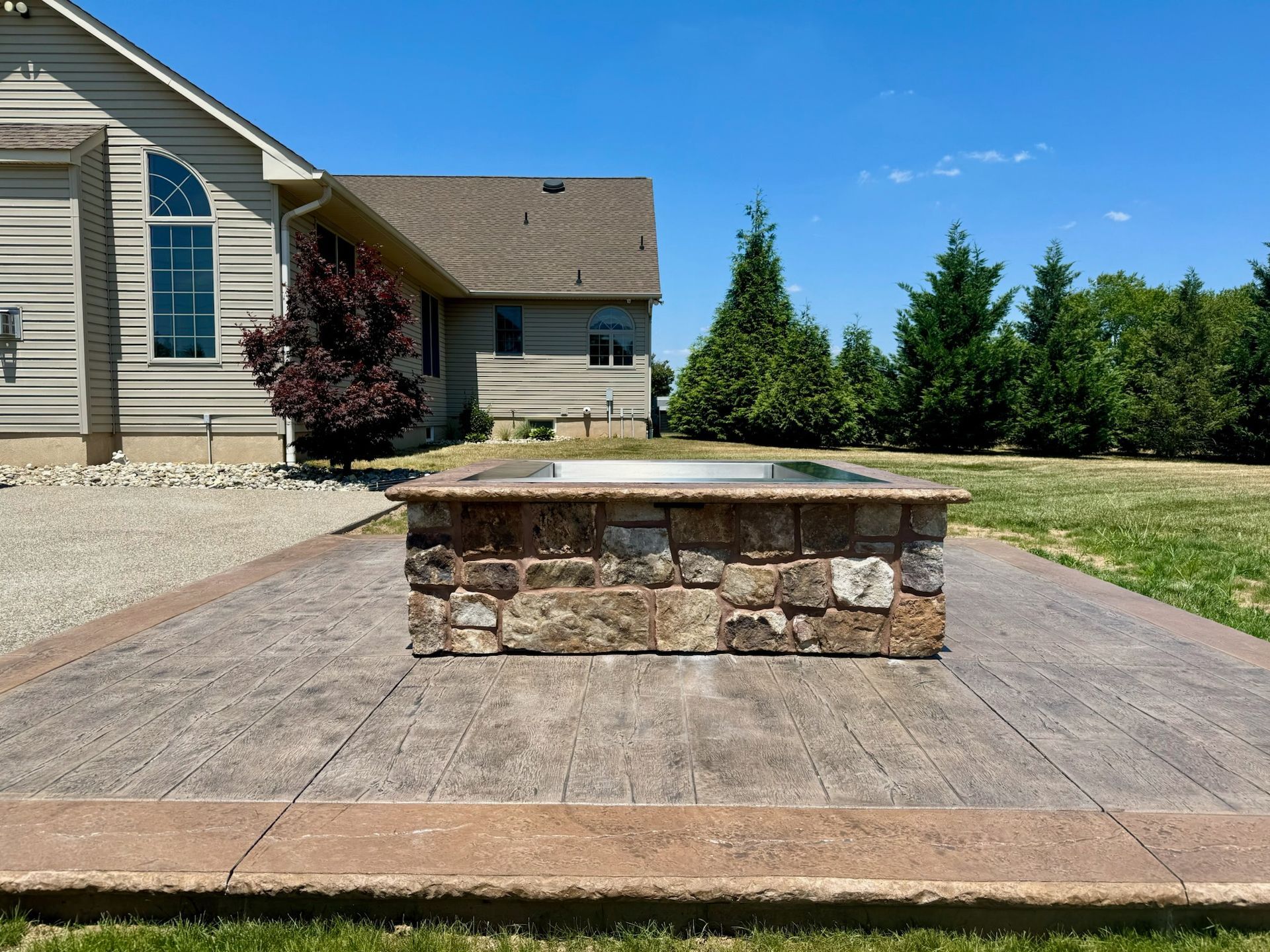 Stone fire pit on a concrete patio in front of a beige house with a green lawn.