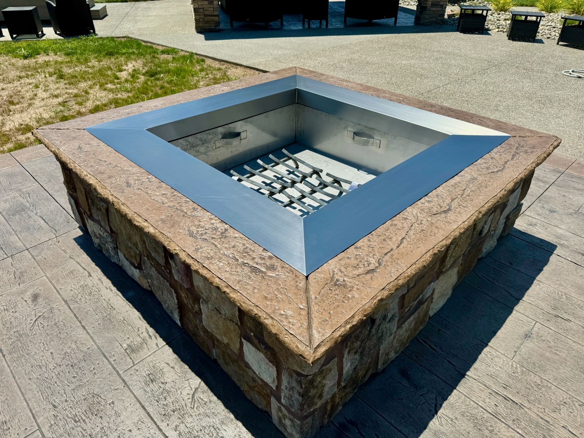 Square fire pit with stone exterior, metal rim, and interior on a concrete patio.