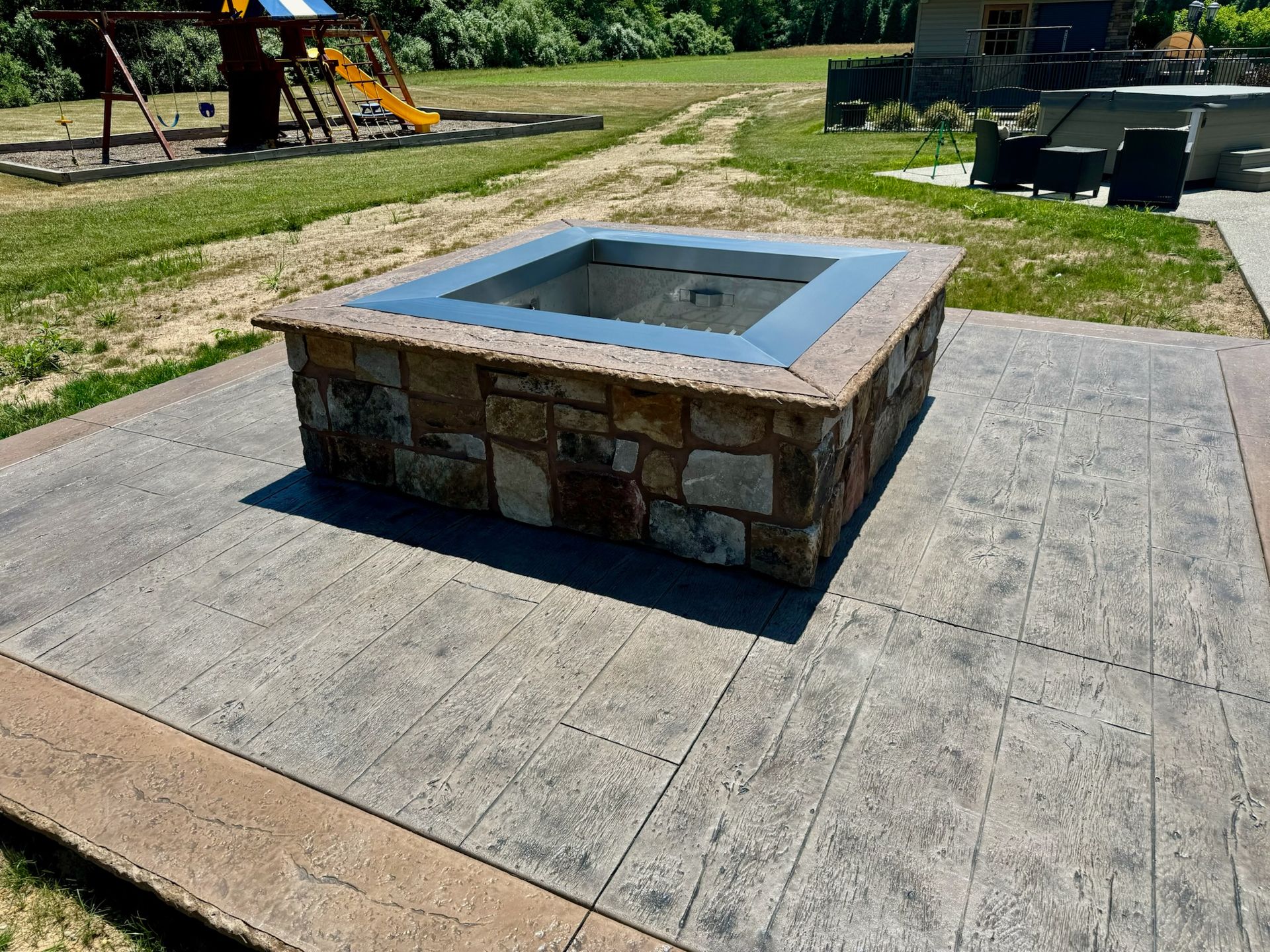 Stone fire pit on a concrete patio, in front of a playground.