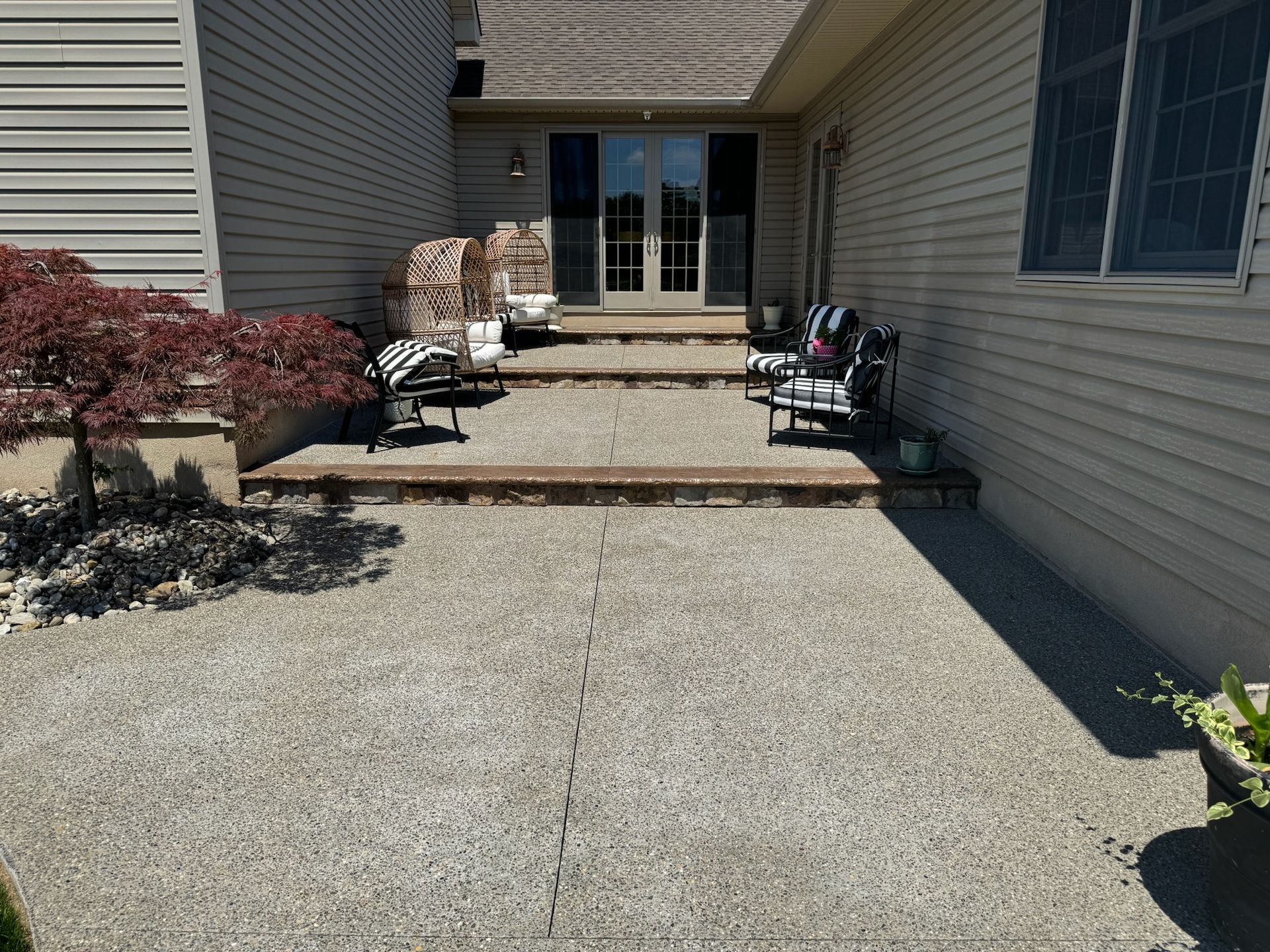 A home's entrance with concrete walkway, steps, two chairs, and a red-leafed tree.