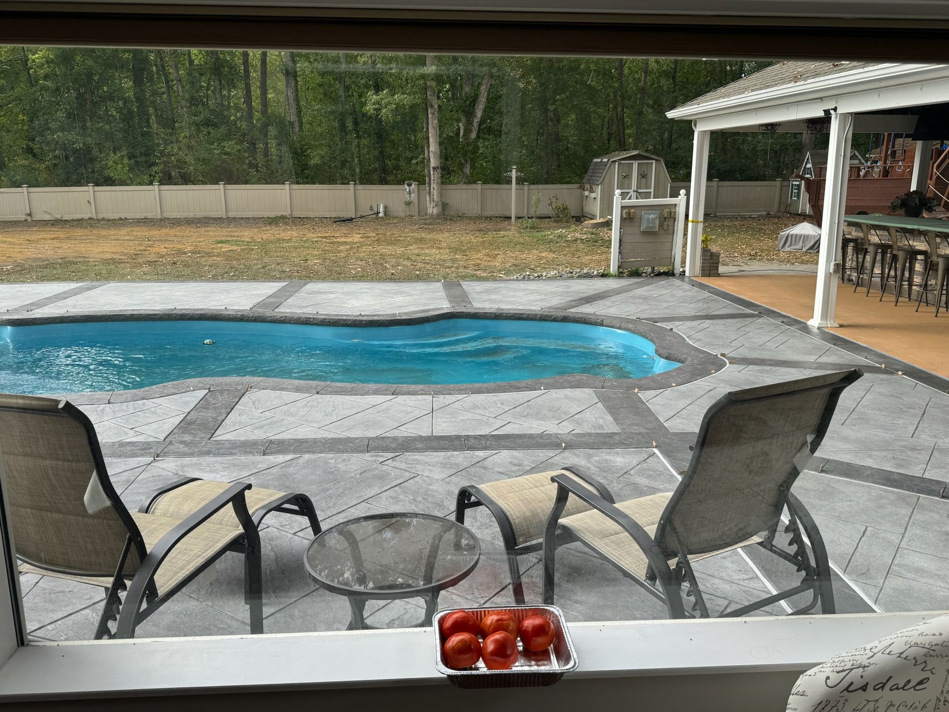 Poolside patio with lounge chairs, small table, and a platter of tomatoes. A blue pool and a bar area are visible.