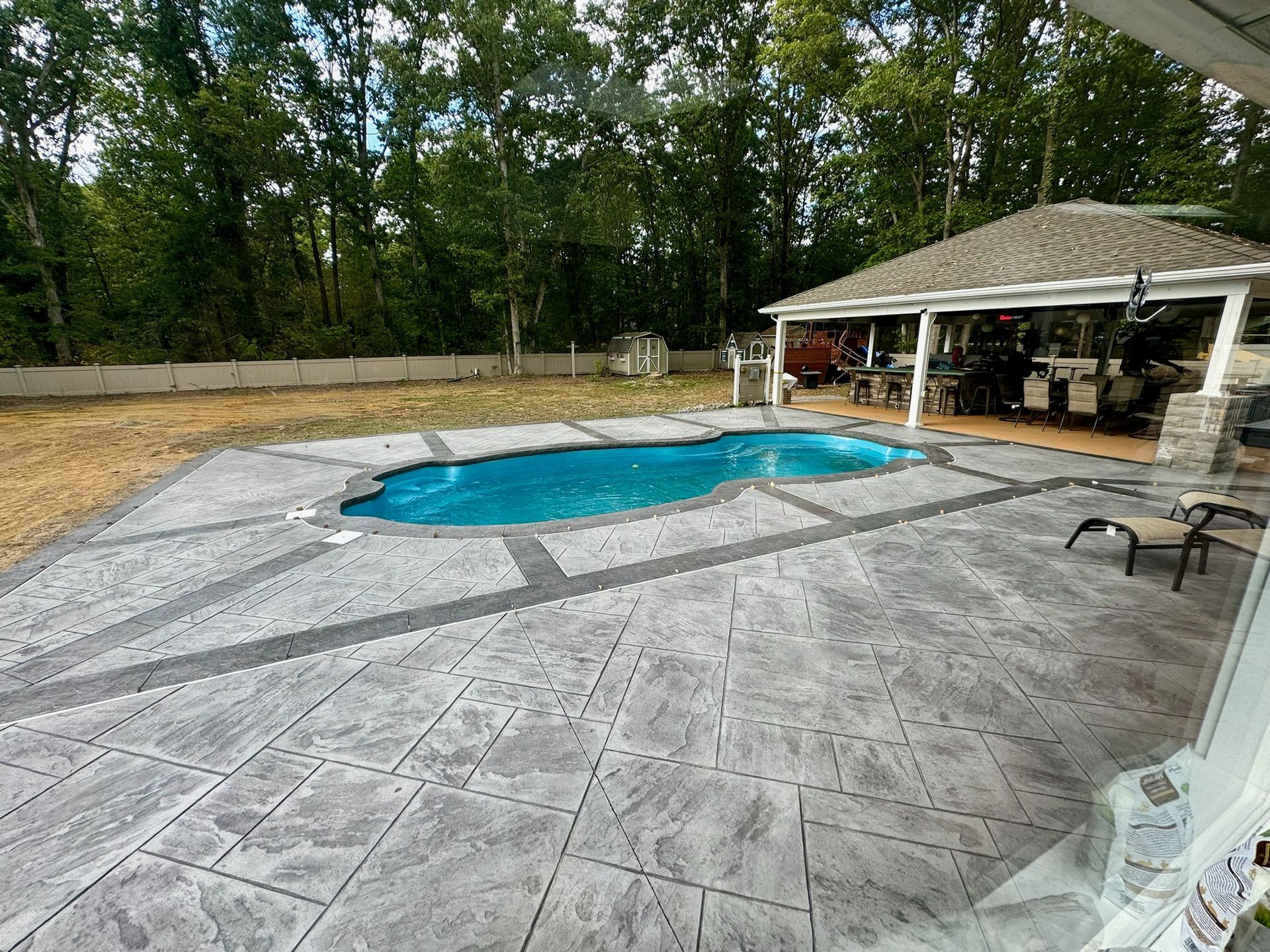 A backyard pool with a gazebo, surrounded by stamped concrete. Trees in the background.