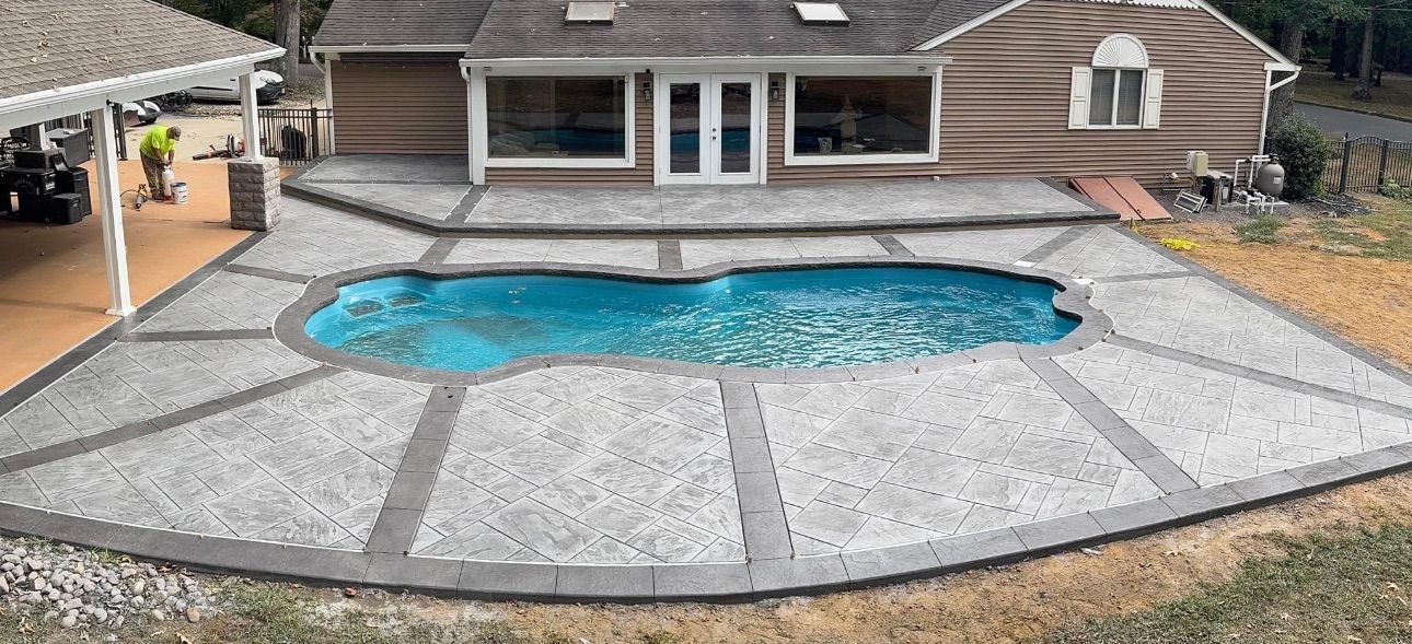 A backyard with a pool surrounded by a gray concrete patio; the house is visible in the background.