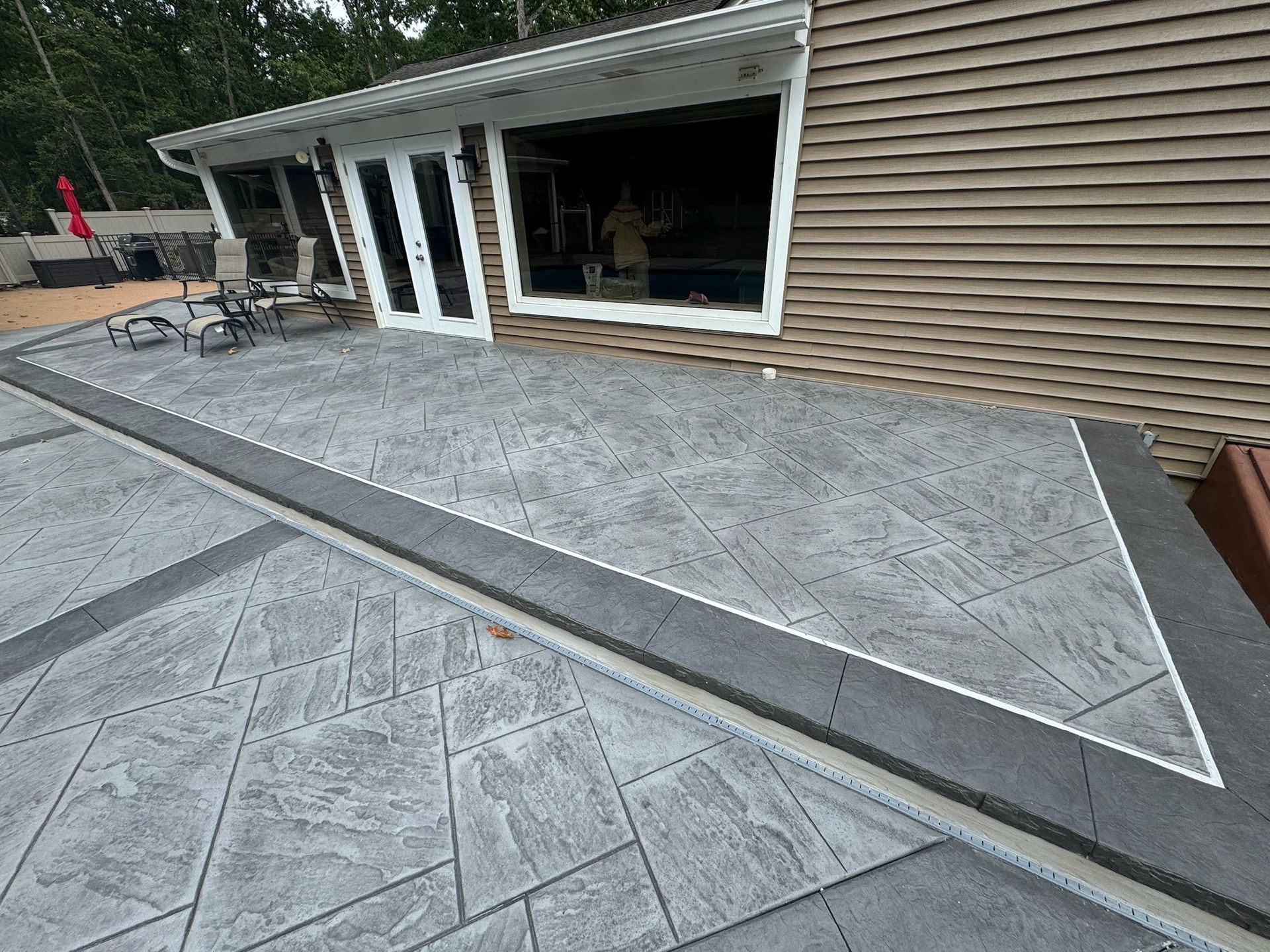 Gray stamped concrete patio with dark border, next to a house with glass doors.