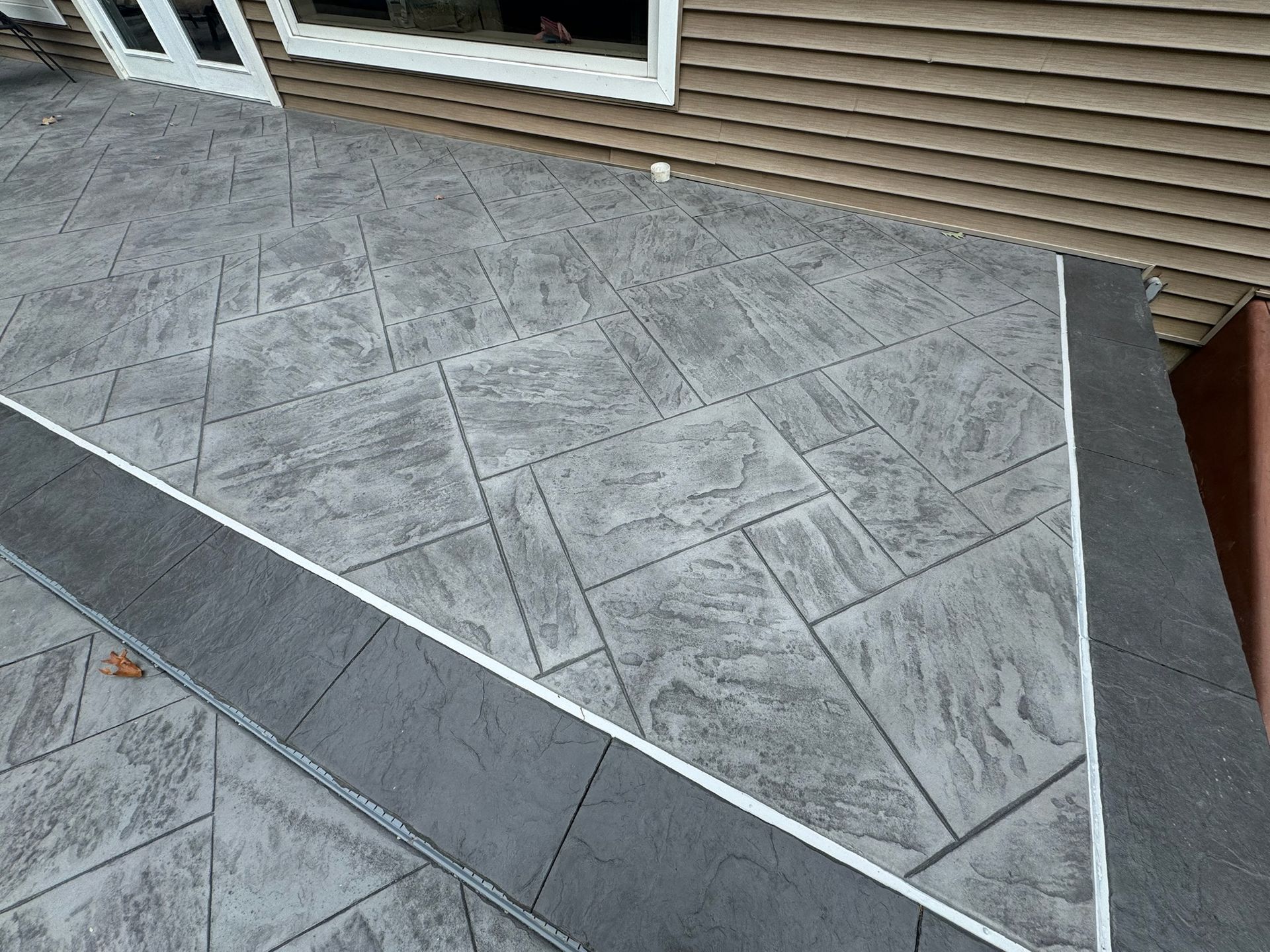 Gray stamped concrete patio with contrasting dark gray border, next to a building's siding.