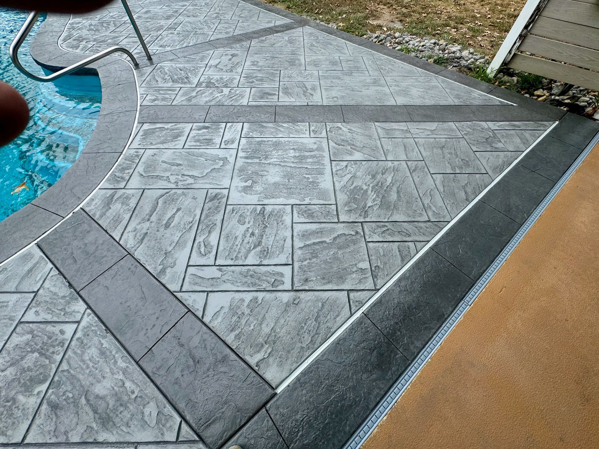Stamped concrete patio with a gray border and textured square patterns surrounding a pool.
