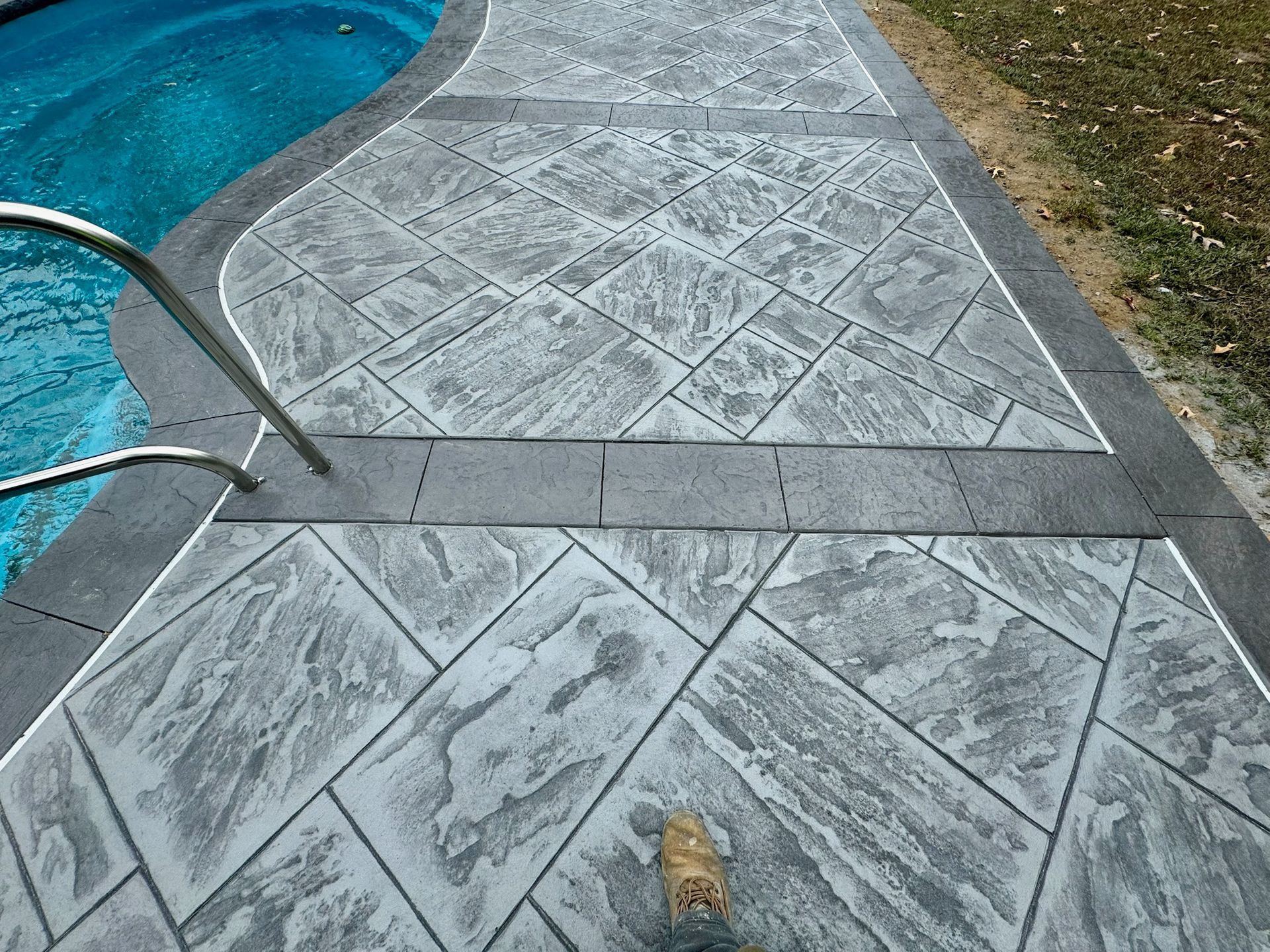 Stamped concrete pool deck with gray geometric pattern and blue pool water.