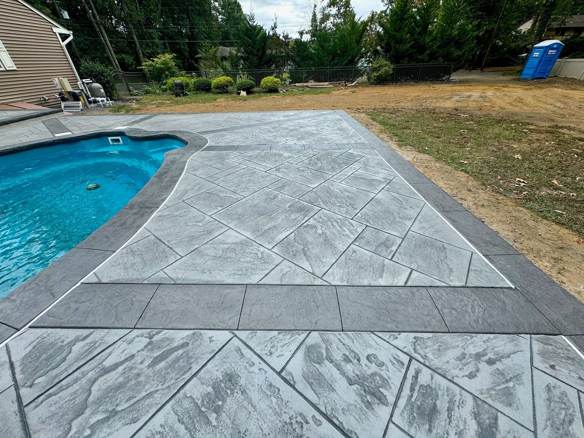 Concrete patio with textured patterns surrounds a pool, framed by green grass and trees.