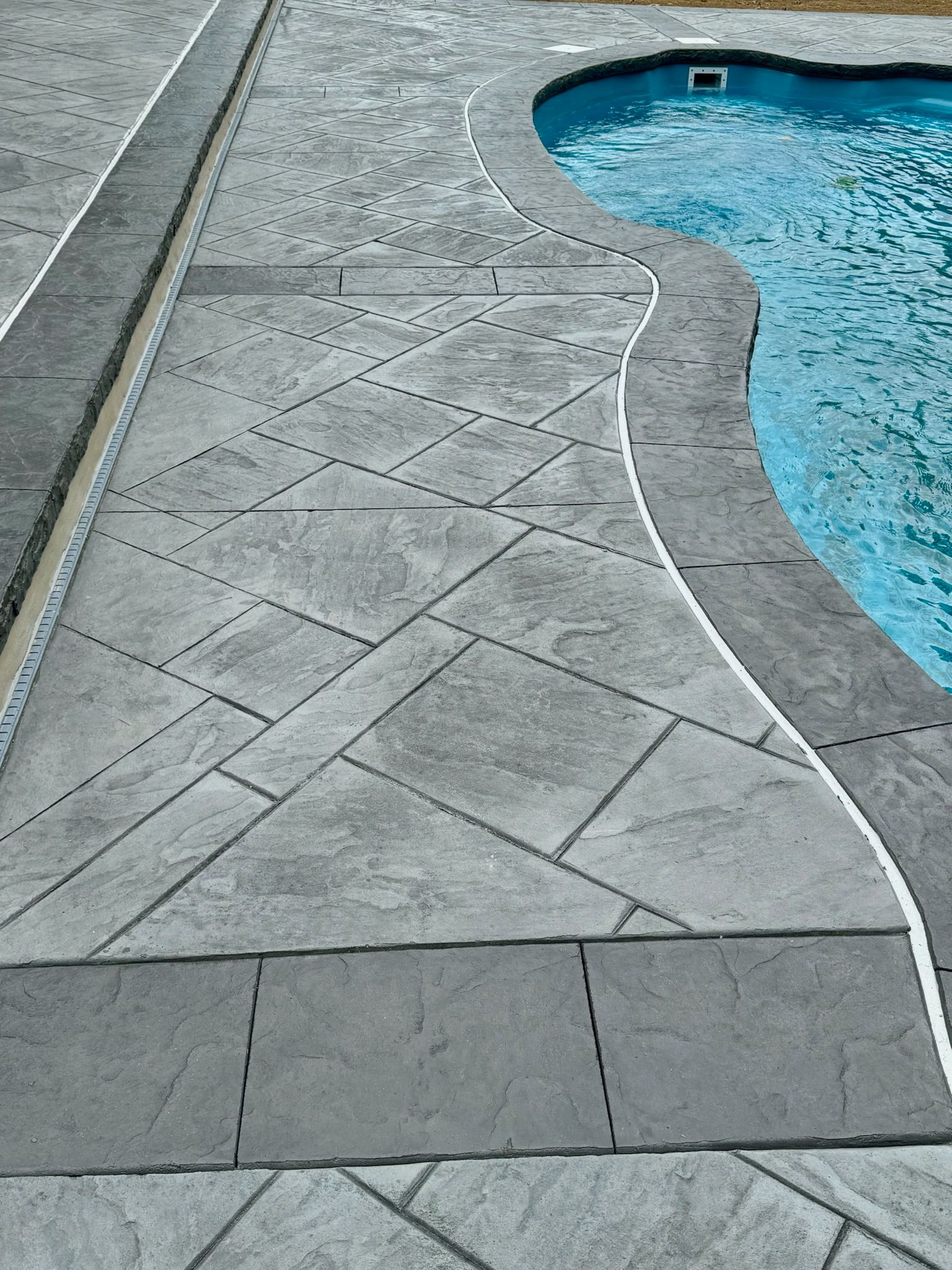 Gray textured concrete pool deck with a curved edge next to a turquoise pool.