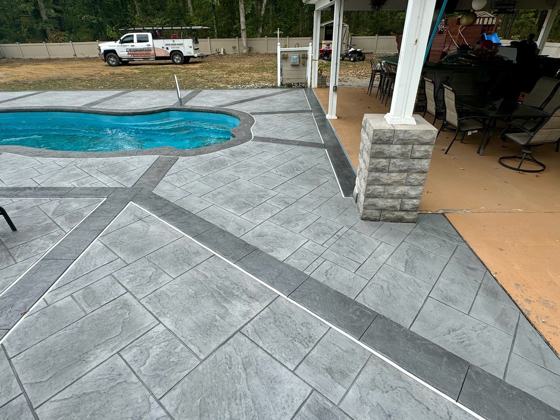 Gray stamped concrete patio with pool, dark grey accents, and white column.