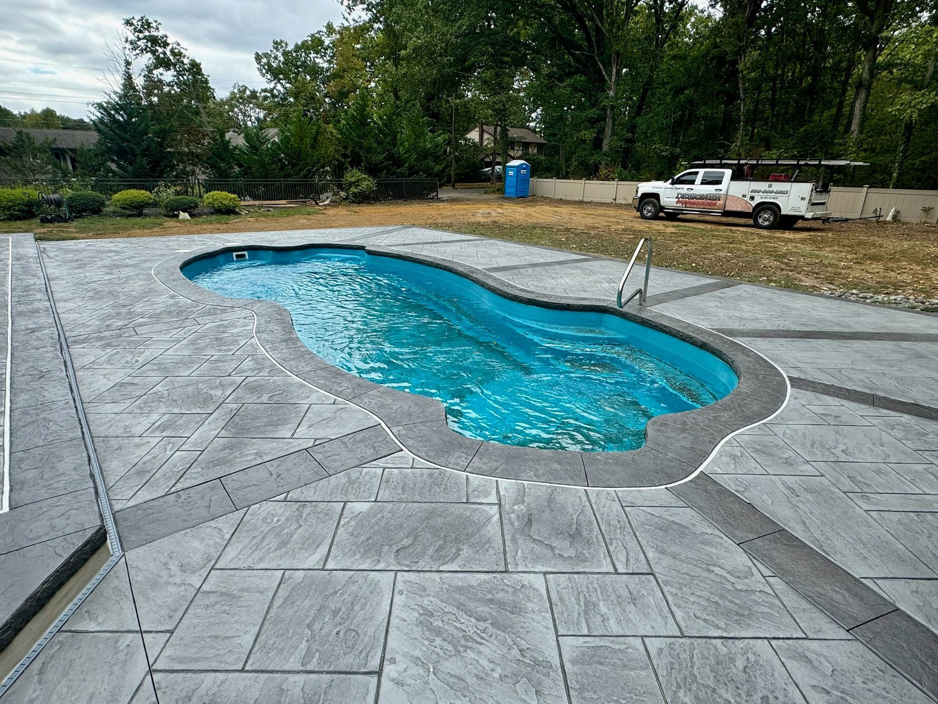 A concrete pool patio with a blue pool, in an outdoor residential setting.