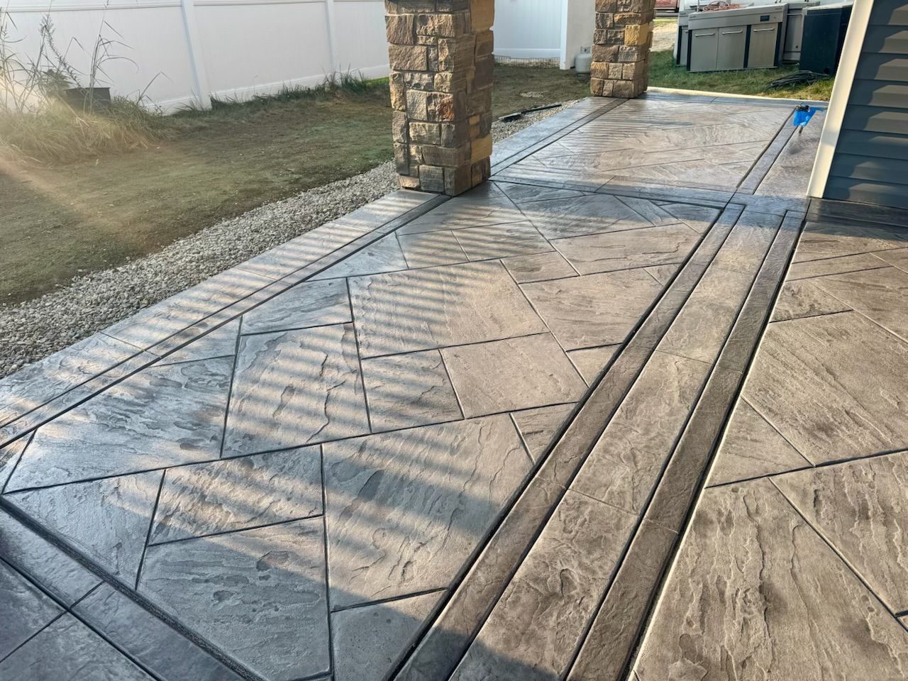 Stamped concrete patio with stone columns, gray textured patterns, and borders.