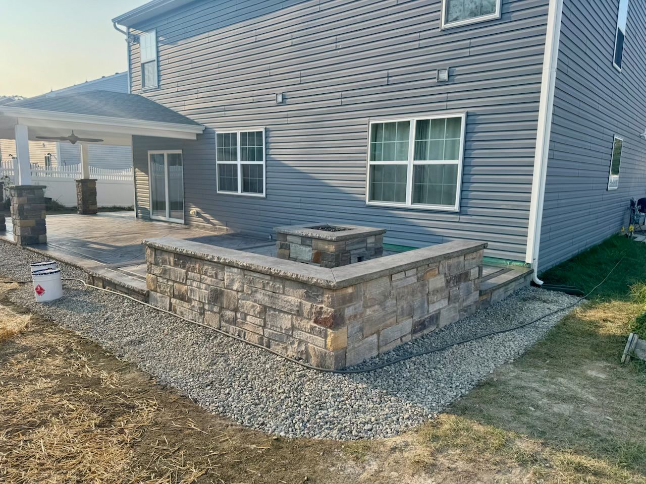 Backyard patio with stone retaining wall, built-in fire pit, and house.