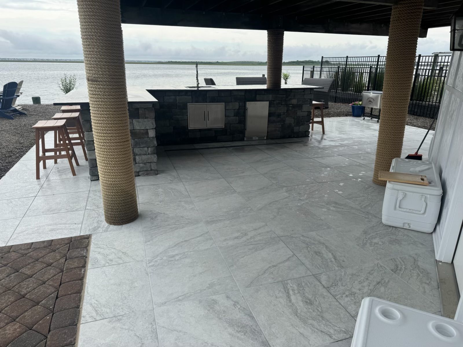 Outdoor patio with a bar, lake view, stone tiles, rope-wrapped pillars, and bar stools.