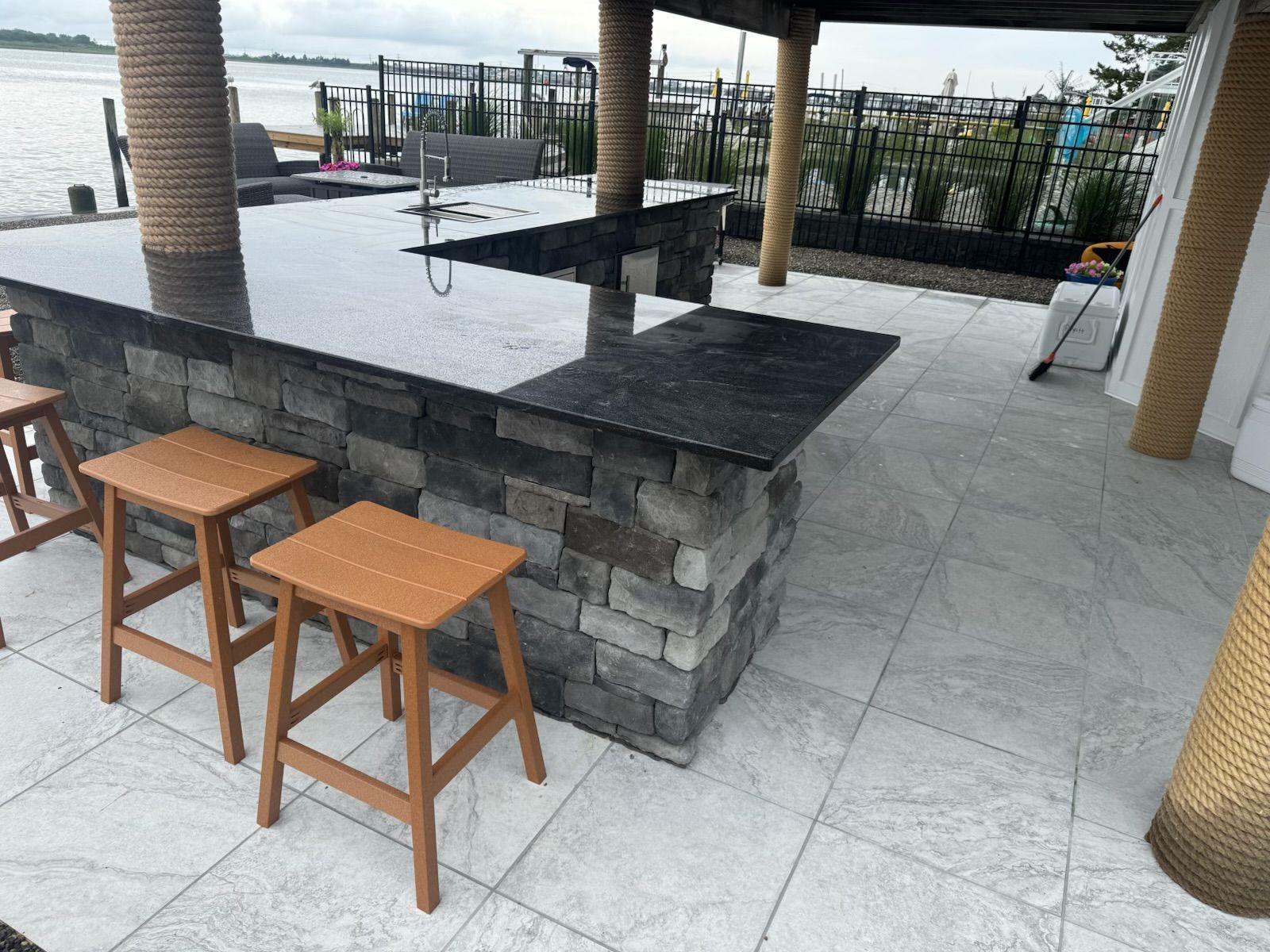Outdoor bar with stone facade and granite countertop, wooden stools.