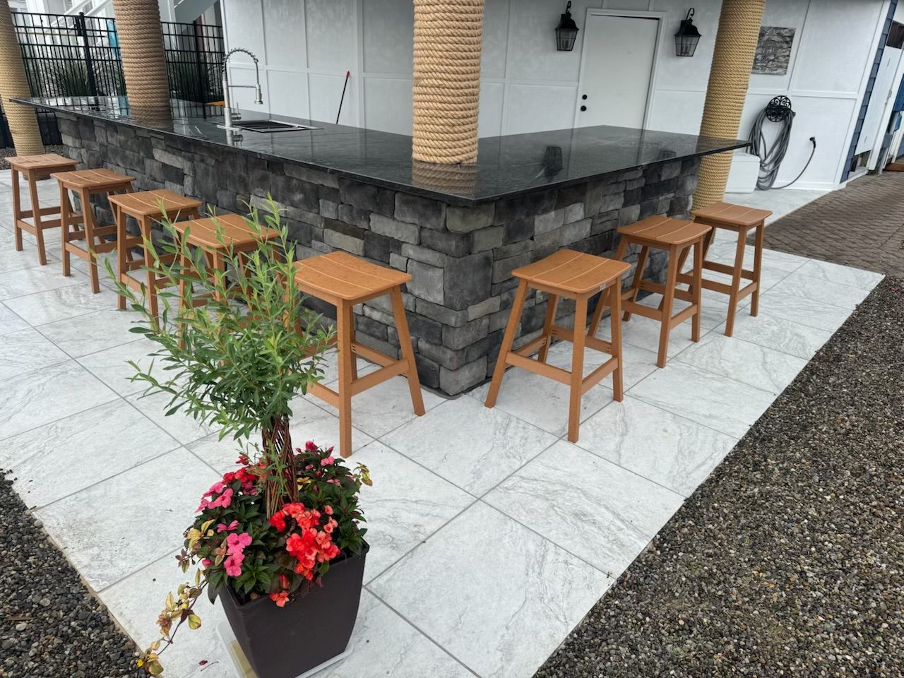 Outdoor bar with stone facade, black countertop, and wooden stools. A potted plant sits in front.