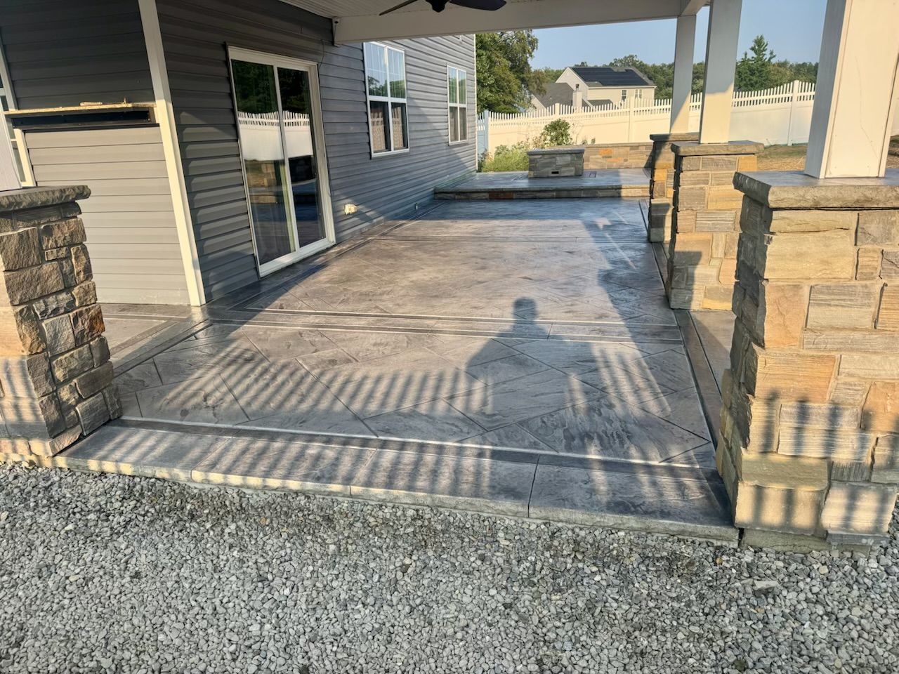 Concrete patio with stone columns, gray siding, and a shadow.