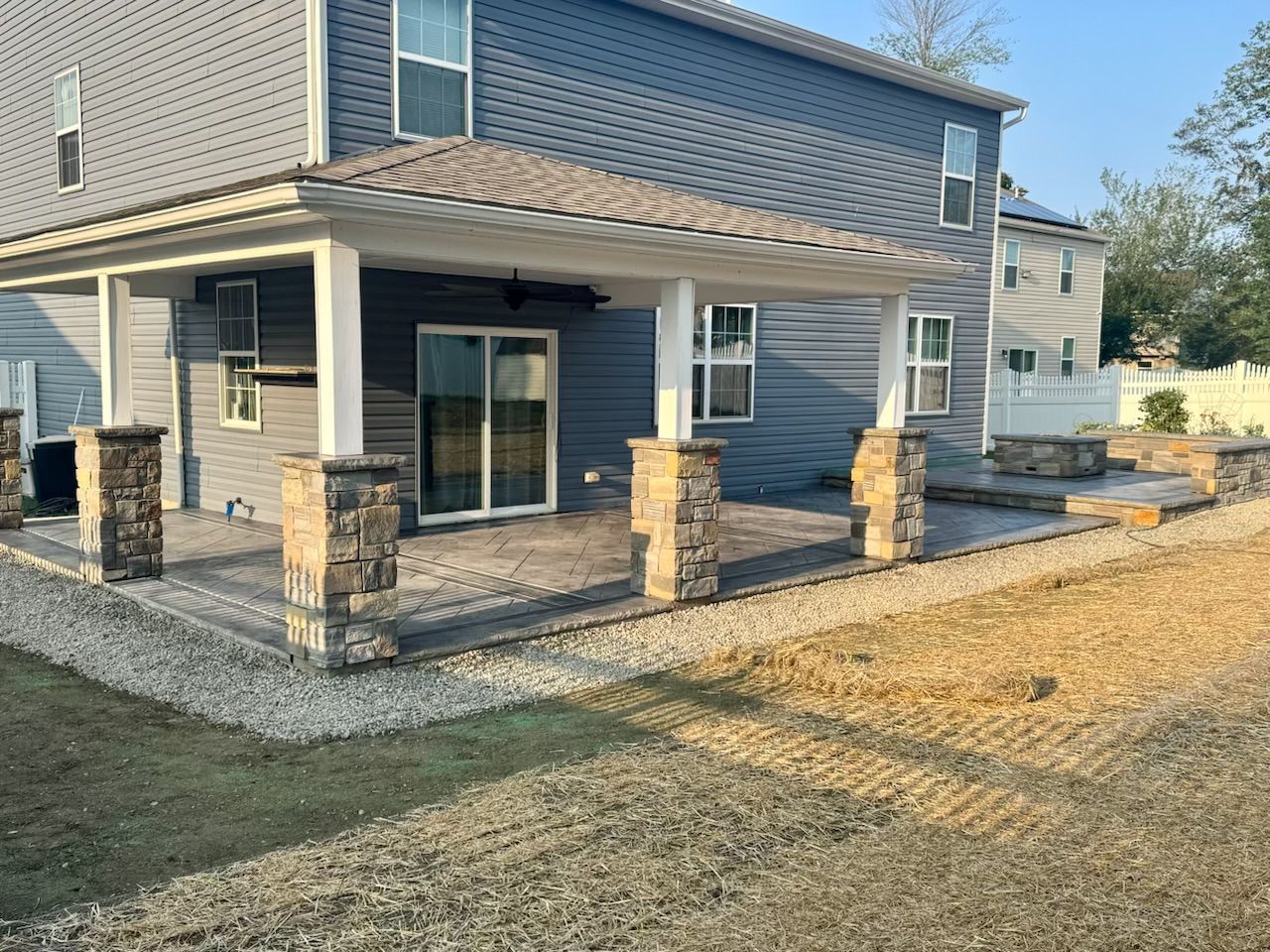 Backyard patio with stacked stone columns, gravel border, and house with blue siding.
