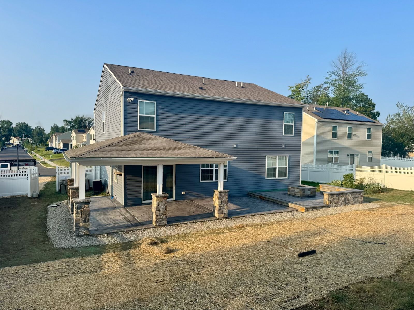 Back of a blue two-story house with a covered patio and a partially landscaped yard.