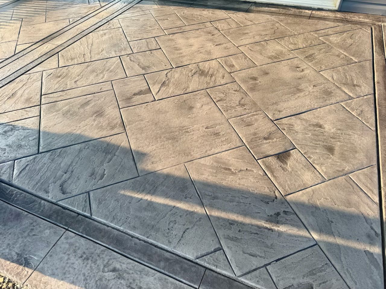Stamped concrete patio with gray stone pattern, dark lines, and sunlight.