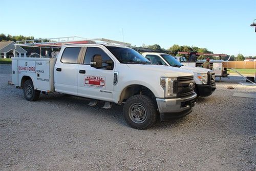 White utility truck parked on gravel lot with trailer attached, under a clear blue sky