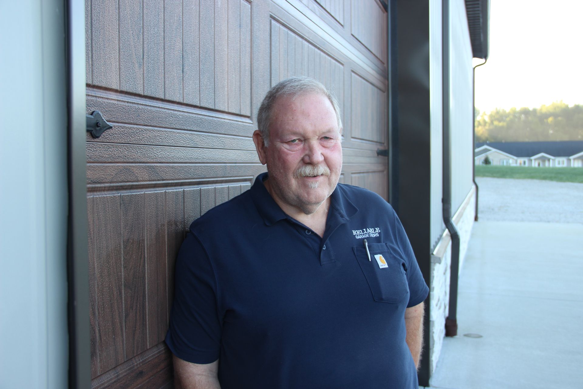 Smiling man in a navy polo shirt leaning against a wooden wall outside a building