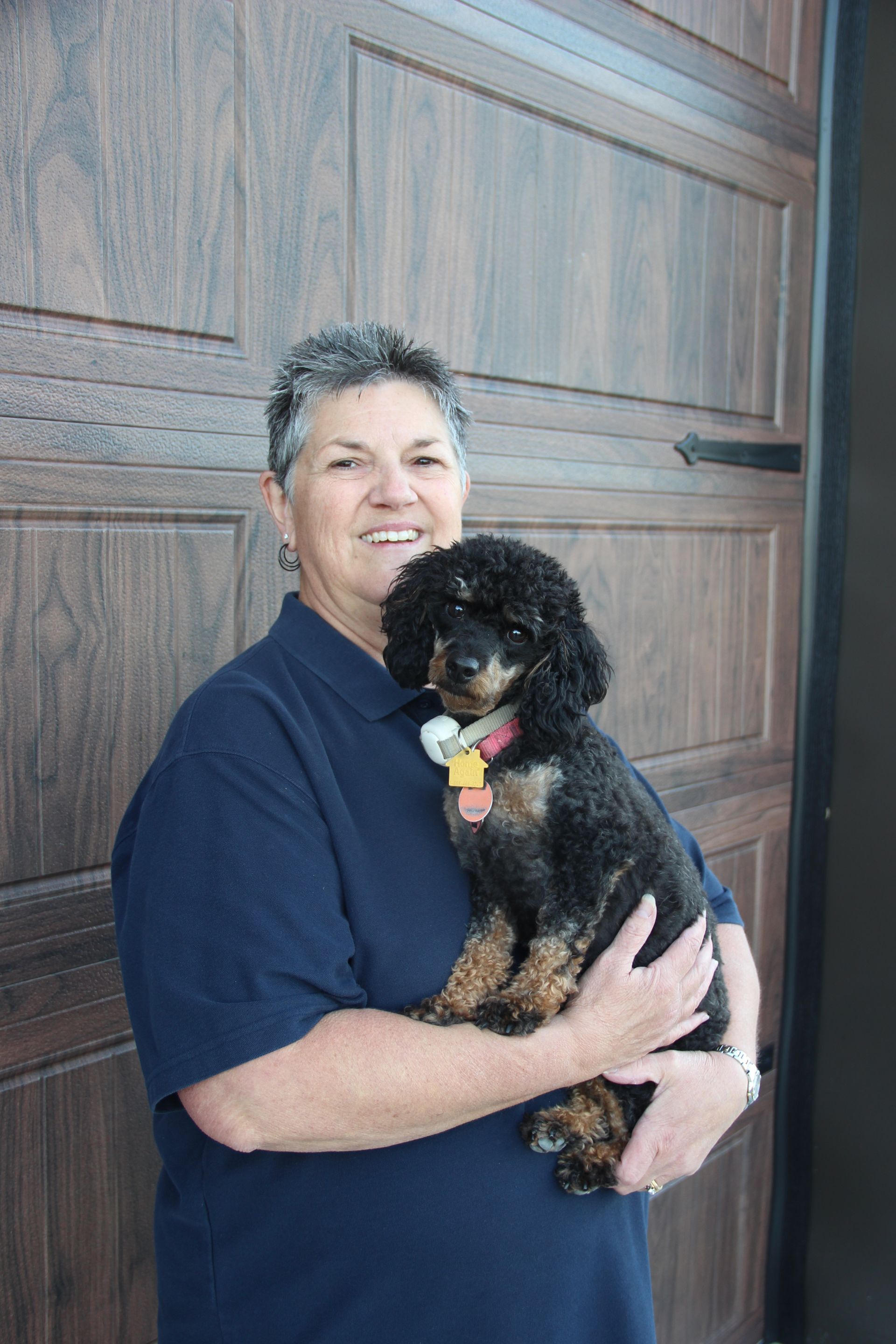 Person holding a small black dog in front of a wooden garage door