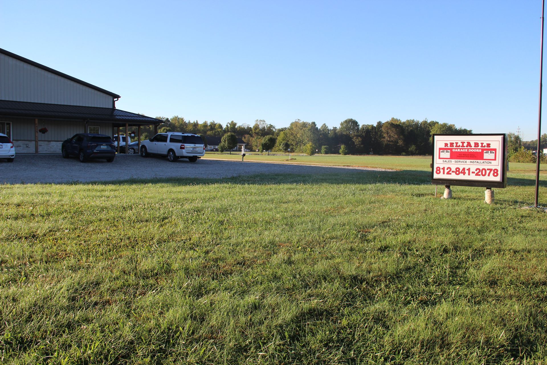 Grassy roadside lot beside a building, with parked vehicles and a real estate sign near the street.
