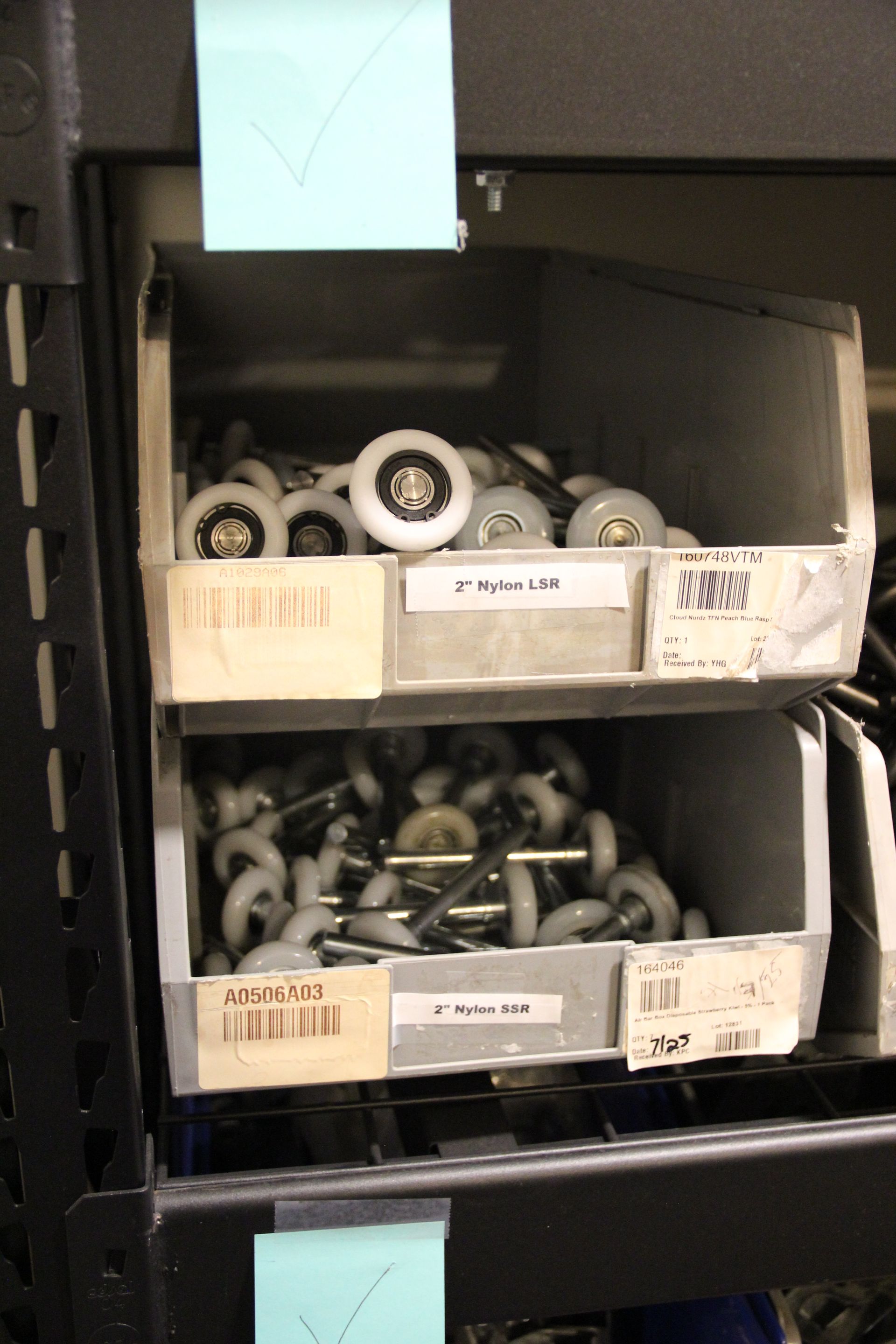 Shelf with two bins of assorted hardware parts and wheels in a storage area.