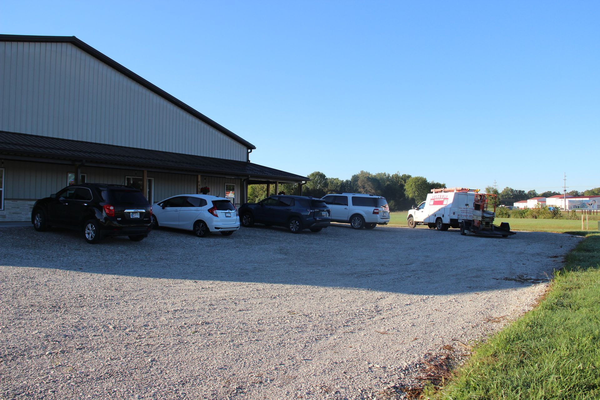 Gravel parking lot beside a metal building with several parked cars and an ambulance in the distance