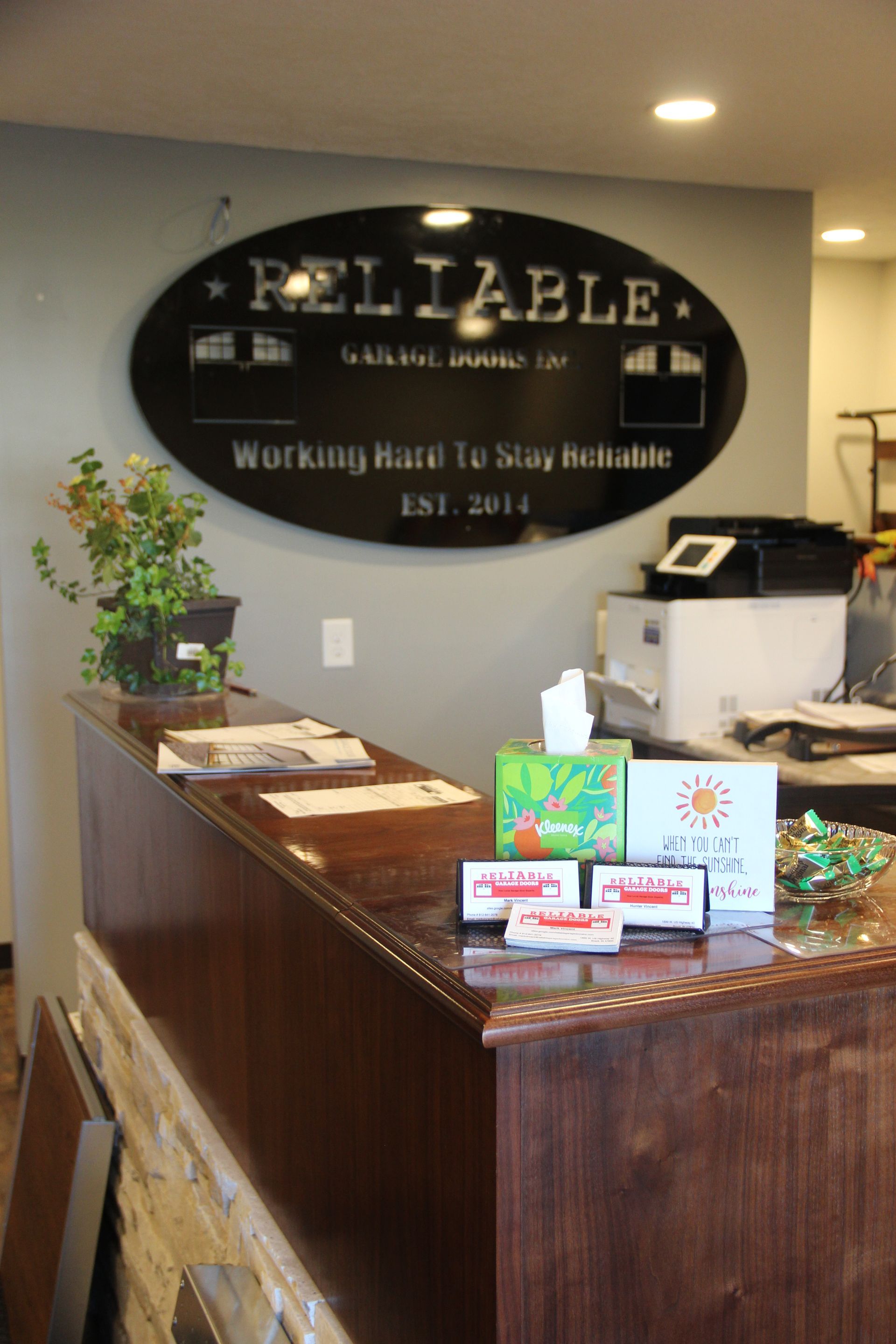 Reception desk in a lobby with a “Reliable” sign, brochures, and a potted plant.