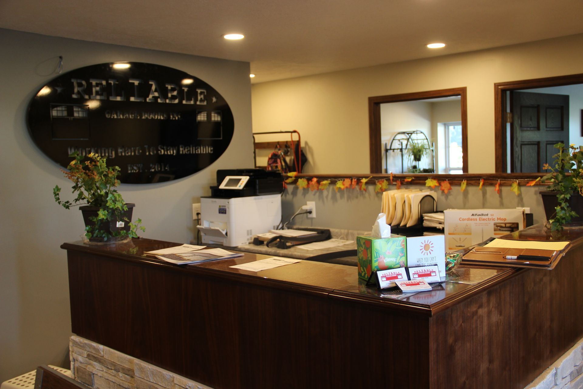 Hotel reception desk with dark wood counter, wall logo, and decorative flowers in a warmly lit lobby