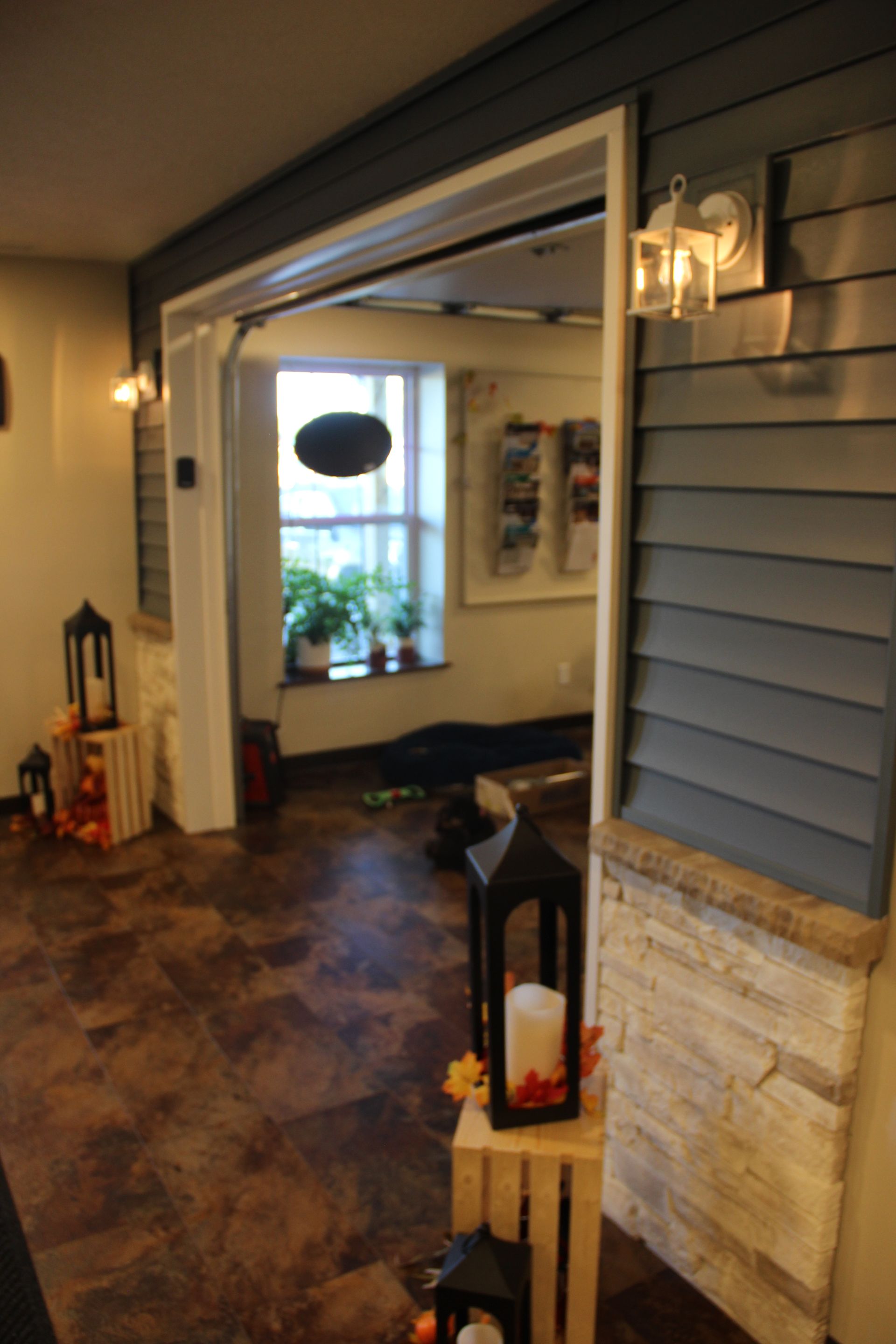 Porch entryway with gray siding, stone base, wall lanterns, and a view into a furnished room beyond.