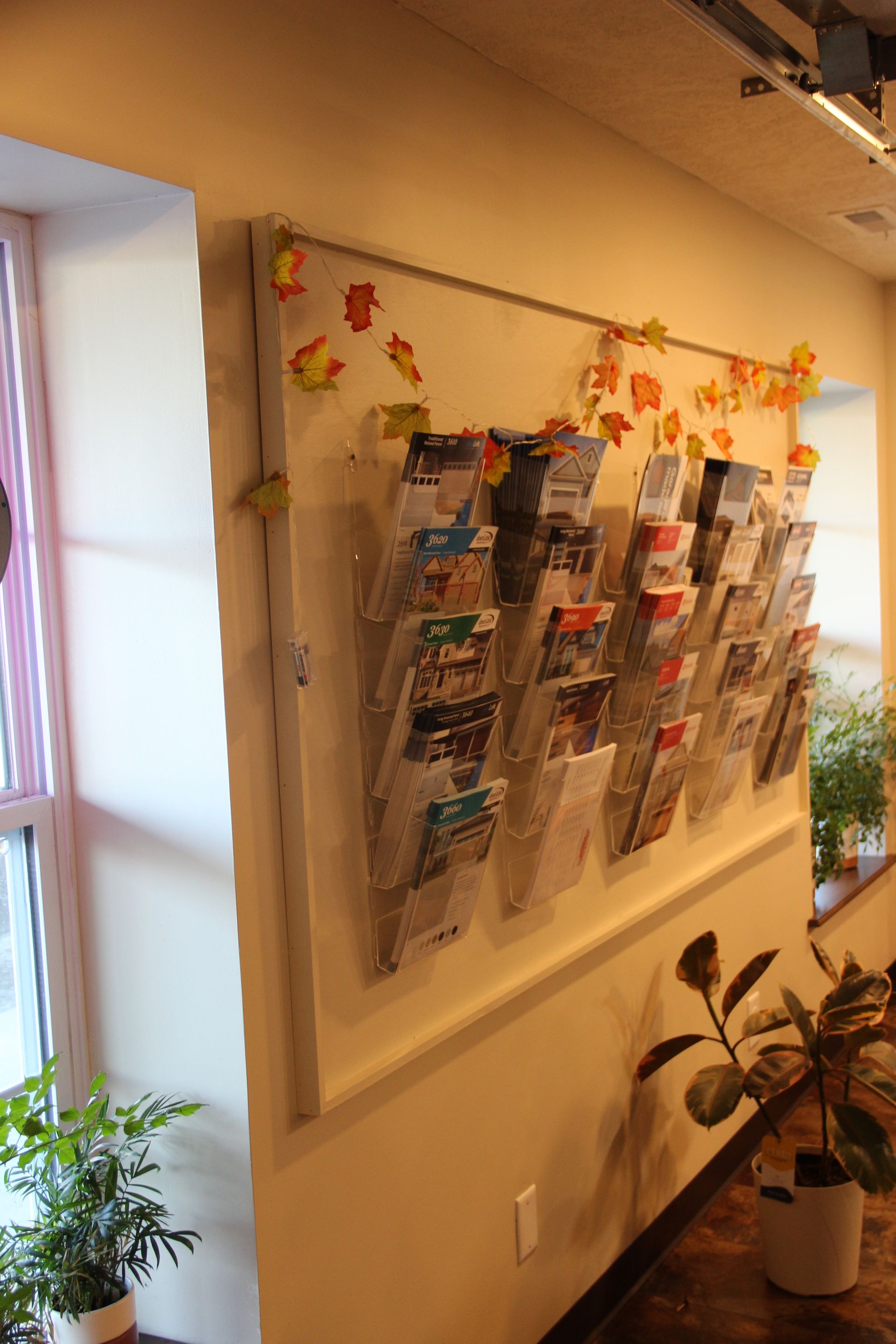 Wall-mounted display rack with brochures and autumn leaf decorations in a bright hallway