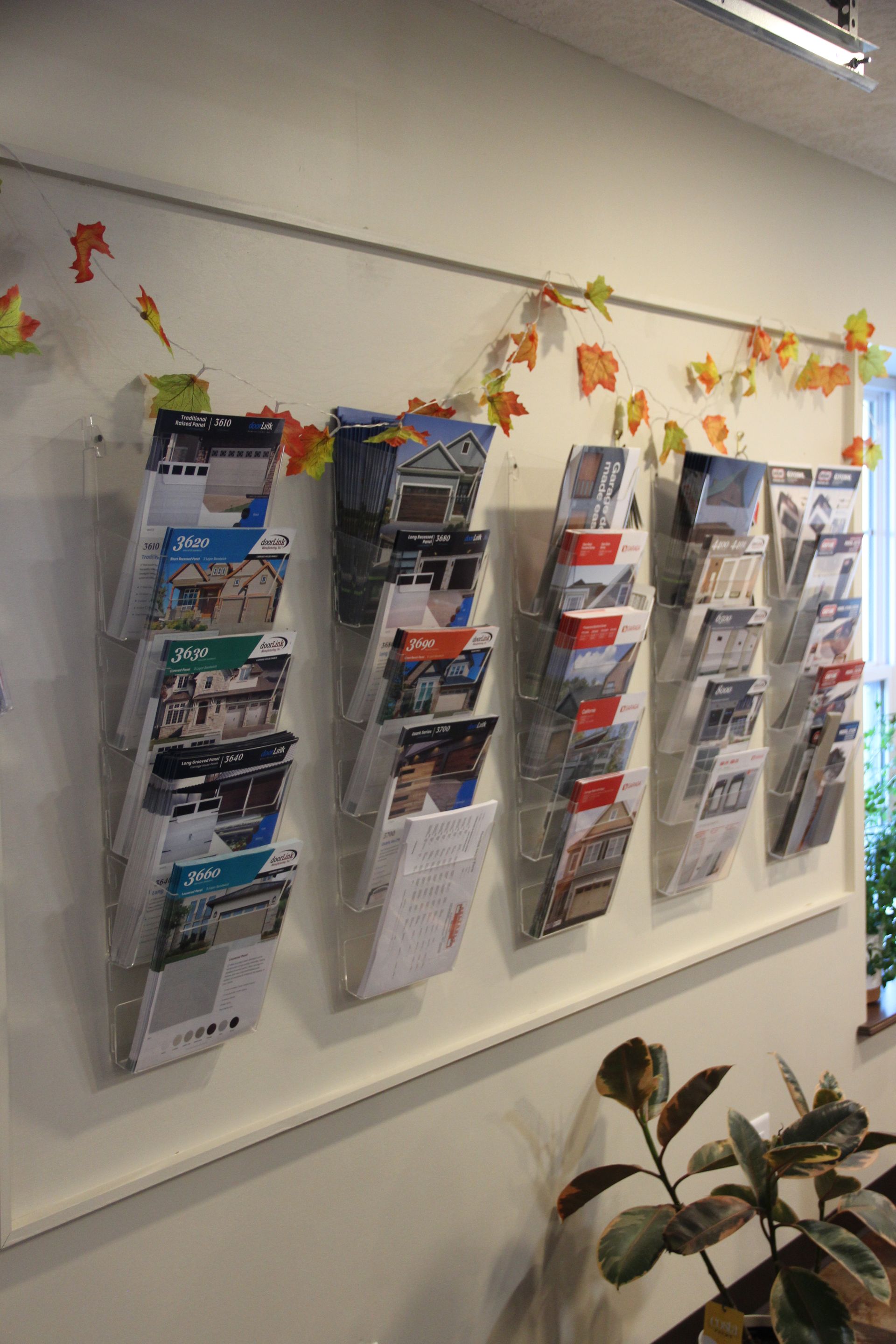 Wall display of magazine racks in a bright office or waiting area, decorated with autumn leaf cutouts.