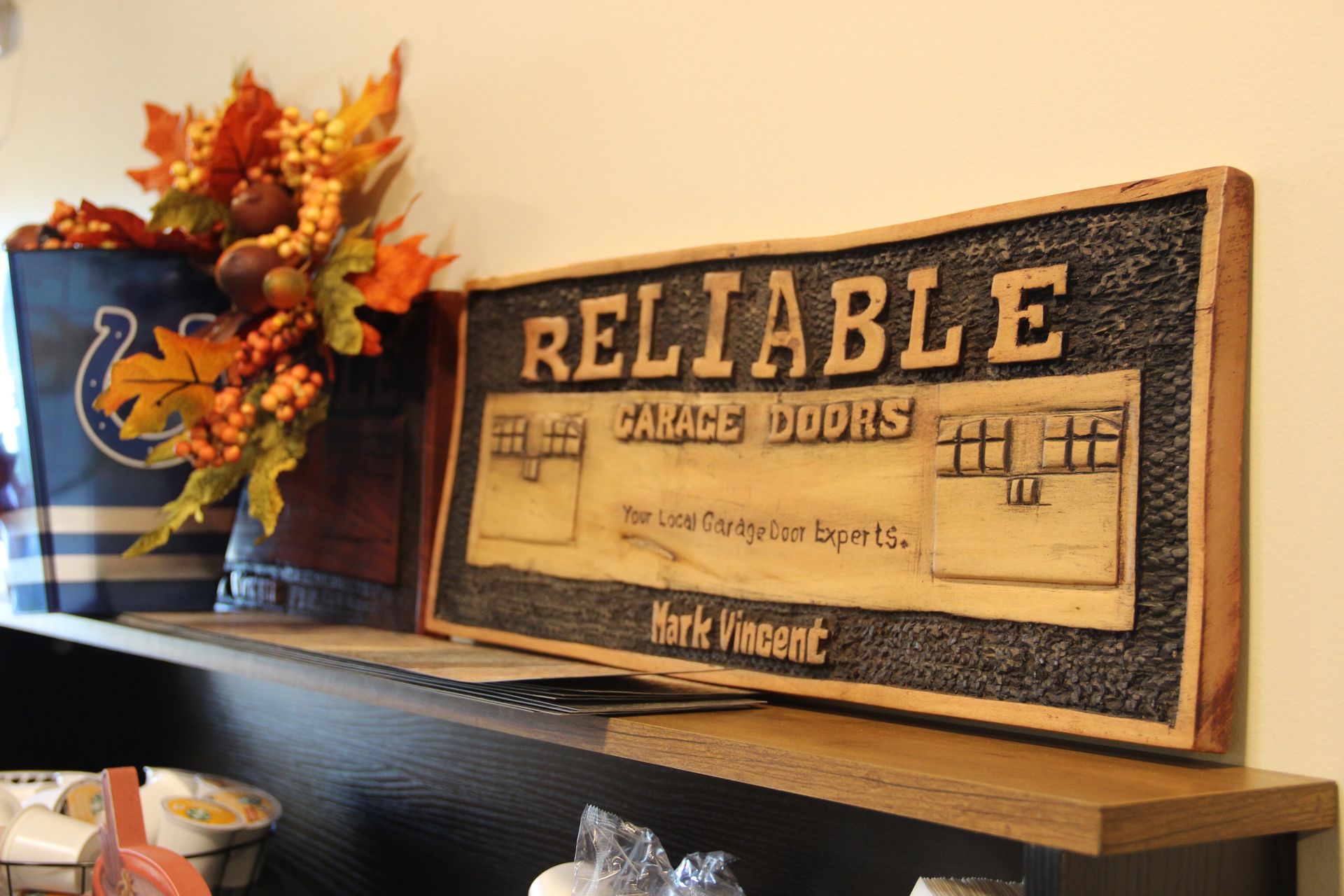 Vintage sign reading “RELIABLE CARPET DOORS” beside a vase of autumn flowers on a shelf