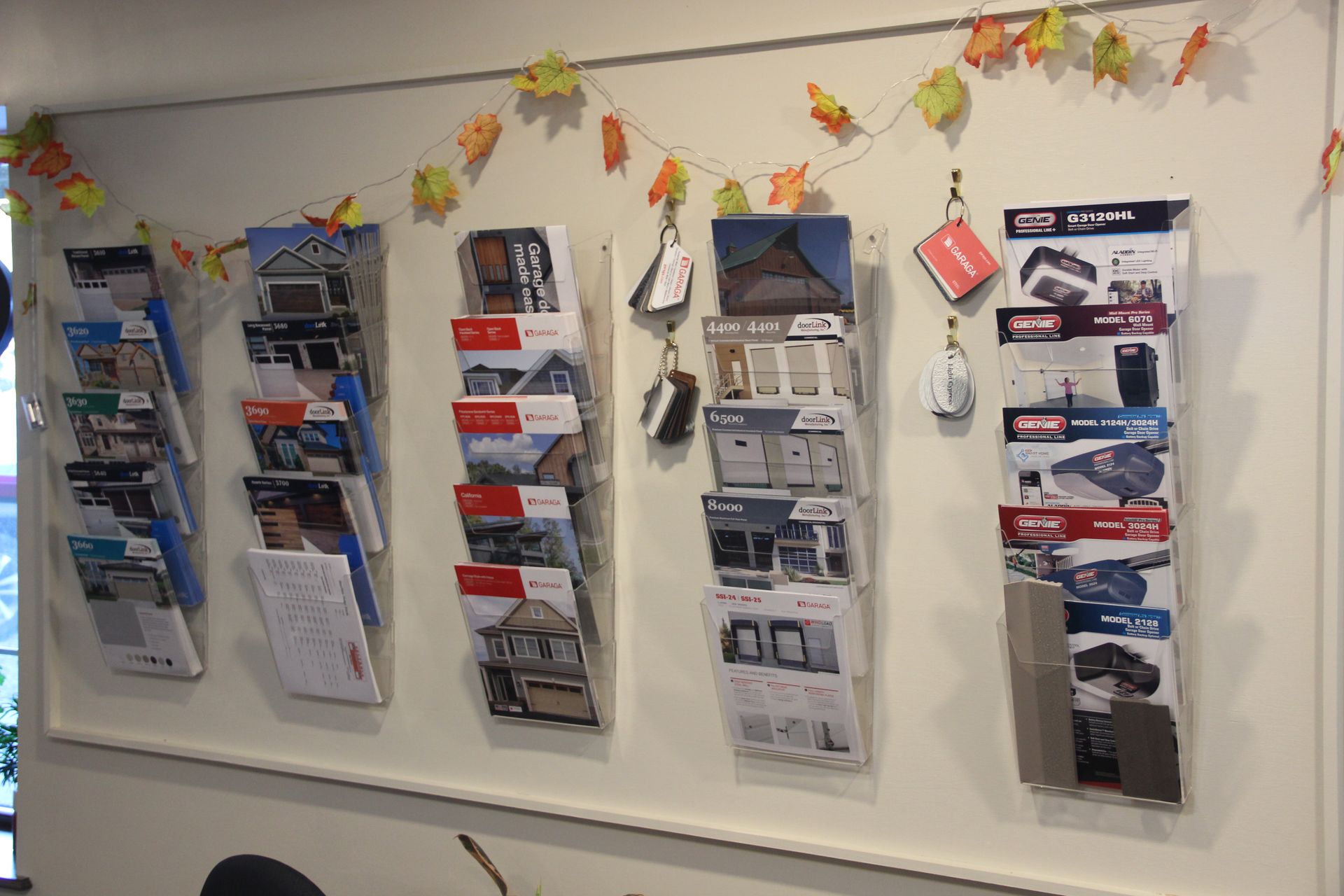 Wall display of pamphlets and brochures in clear holders, decorated with autumn leaf garland