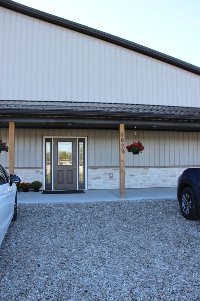 Front entrance of a white building with a gray door, gravel driveway, and hanging flower basket.