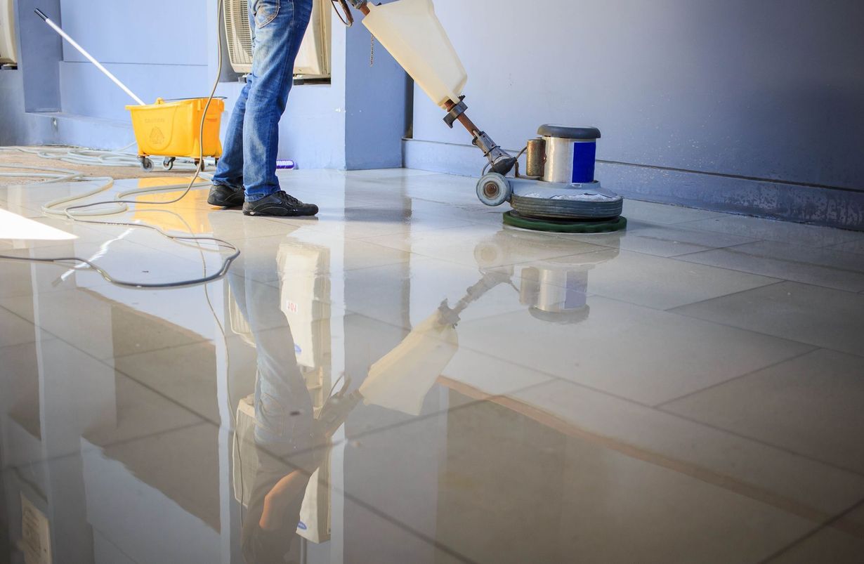 A person uses a floor buffer machine to polish a reflective, clean tile floor.
