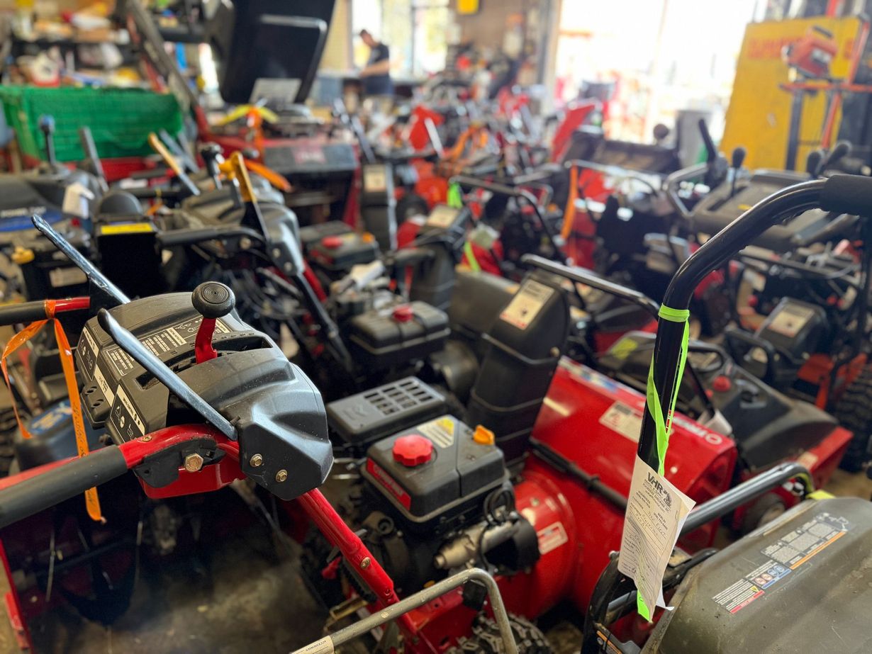 A cluttered showroom filled with rows of red and black snow blowers for sale.