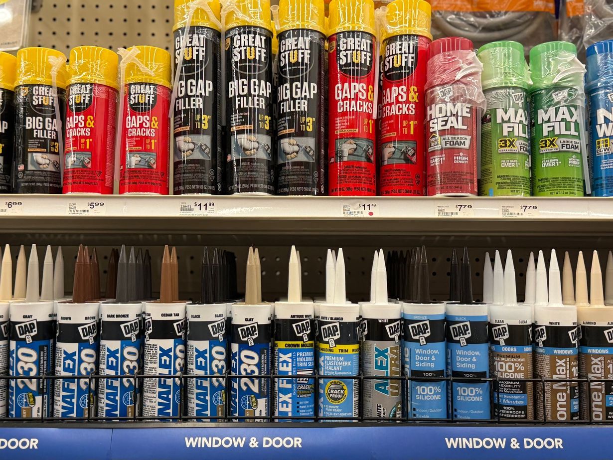 Store shelves stocked with rows of aerosol spray foam cans and various tubes of sealant caulking.