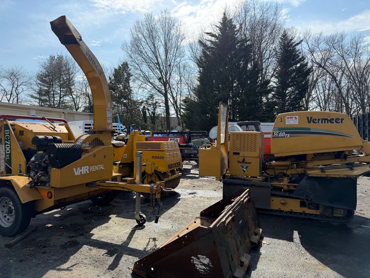 Two yellow Vermeer industrial wood chippers sit in a gravel lot on a sunny day.