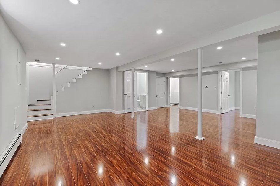 An empty basement with hardwood floors and white walls.
