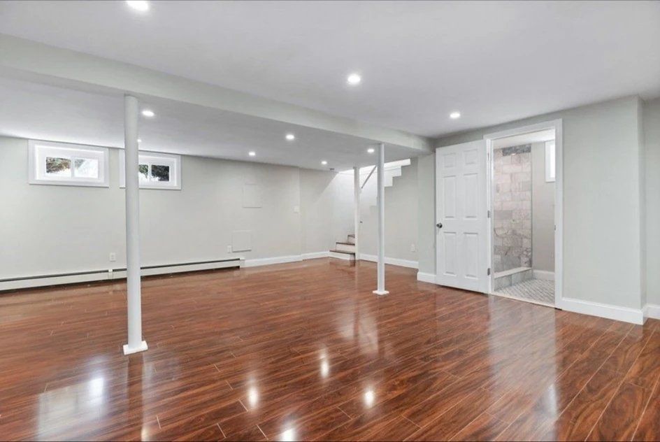 An empty basement with hardwood floors and white walls.