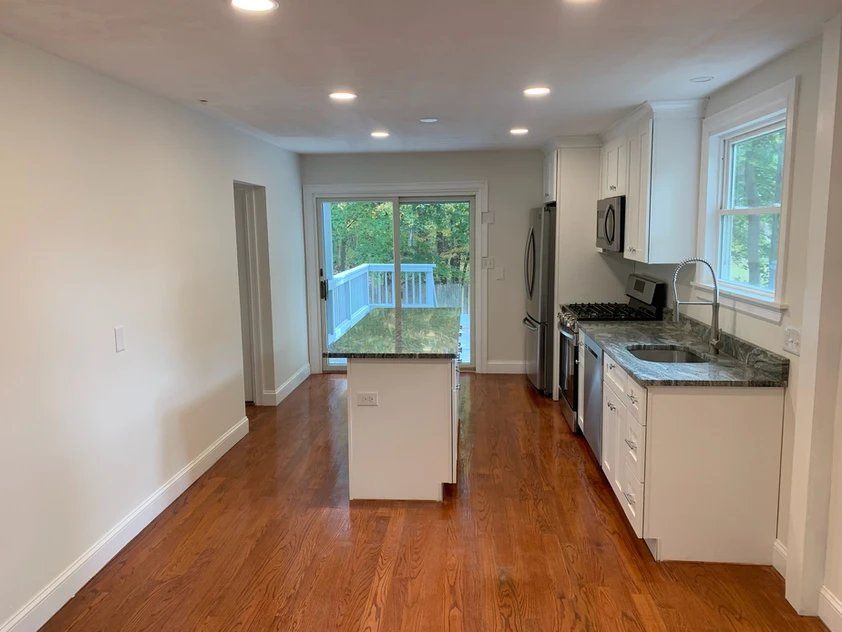 An empty kitchen with hardwood floors and white cabinets.