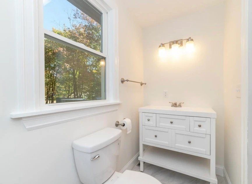 A bathroom with a toilet, sink, and window.
