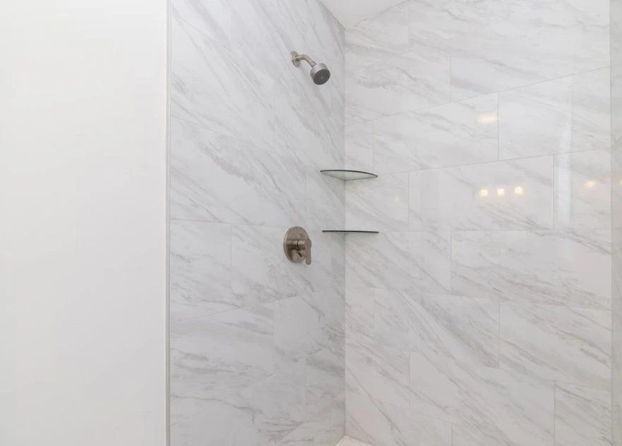 A bathroom with a walk in shower with marble tiles and shelves.