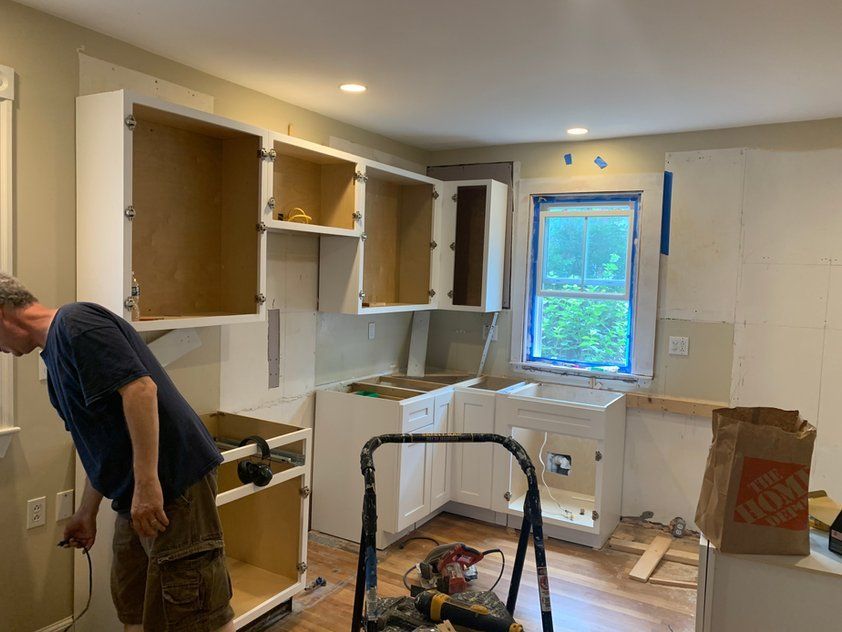 A man is standing in a kitchen looking at cabinets.