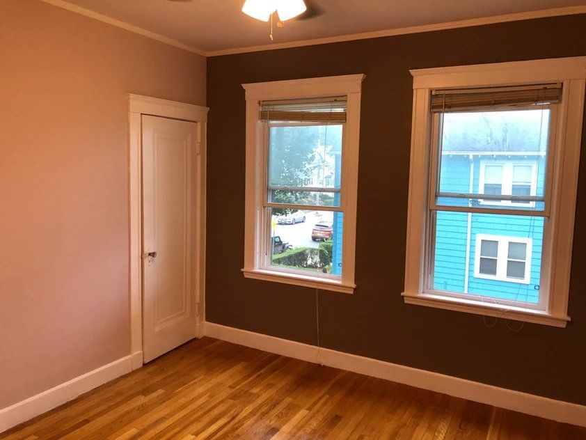 An empty room with two windows and a blue house in the background.
