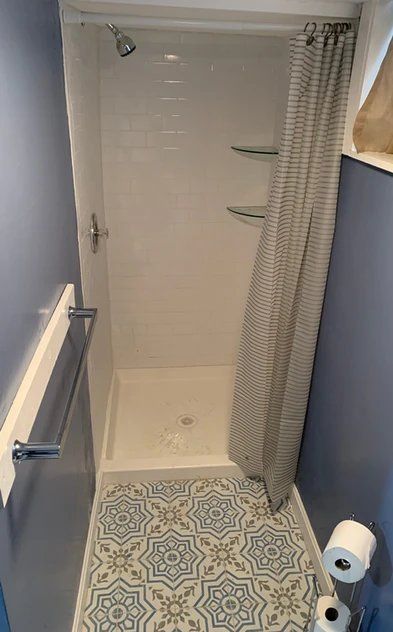 A bathroom with a shower, toilet paper, and tile floor.
